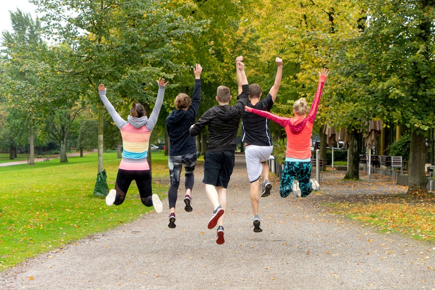 5 junge Sportler springen im Park vor Freude in die Luft